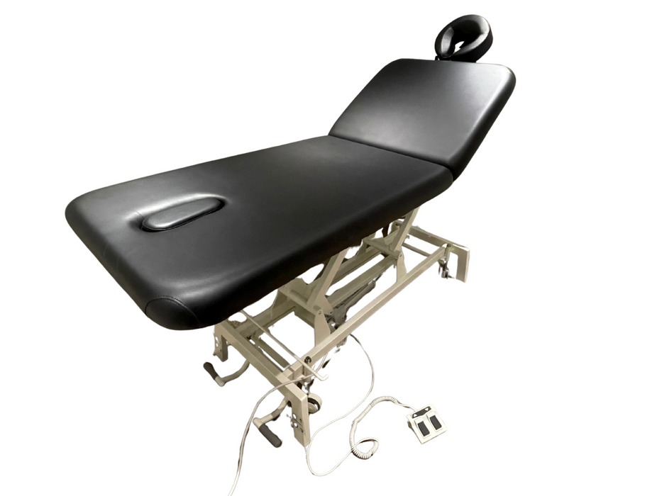Angled view of the 2-section electric treatment table in a fully flat position, highlighting its sturdy white scissor-lift base and comfortable black cushioning.