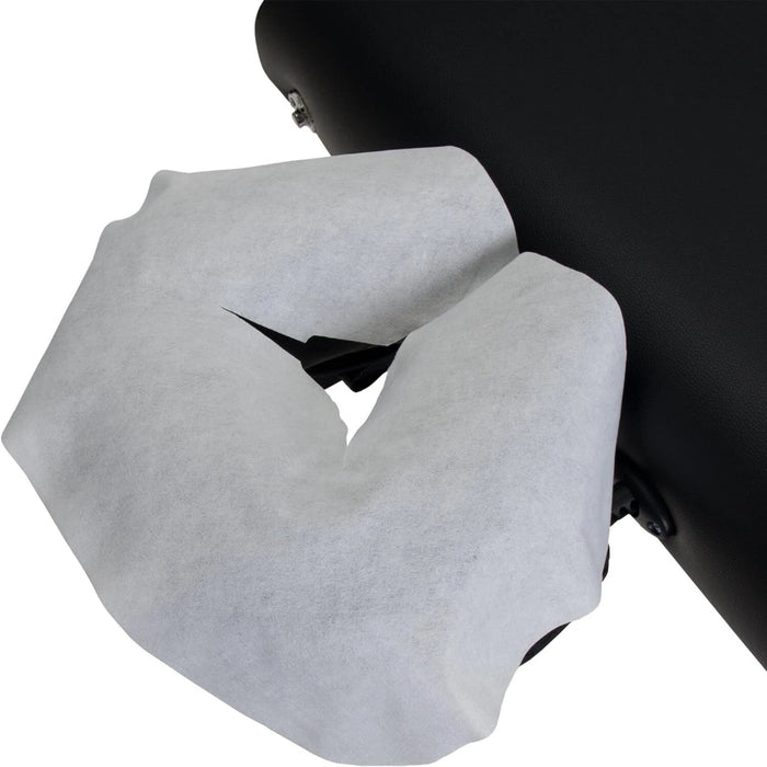 A white disposable face cradle cover shown fitted over a black massage table headrest, illustrating its secure and convenient fit.