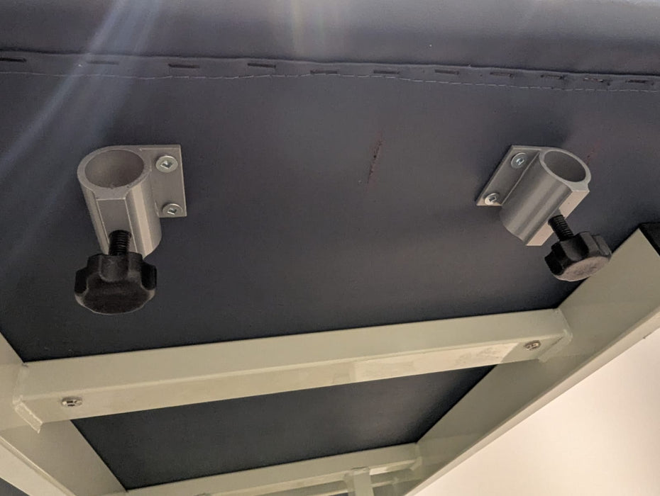 Underside view of a massage table showing two aluminum face cradle bracket mounts with thumbscrews