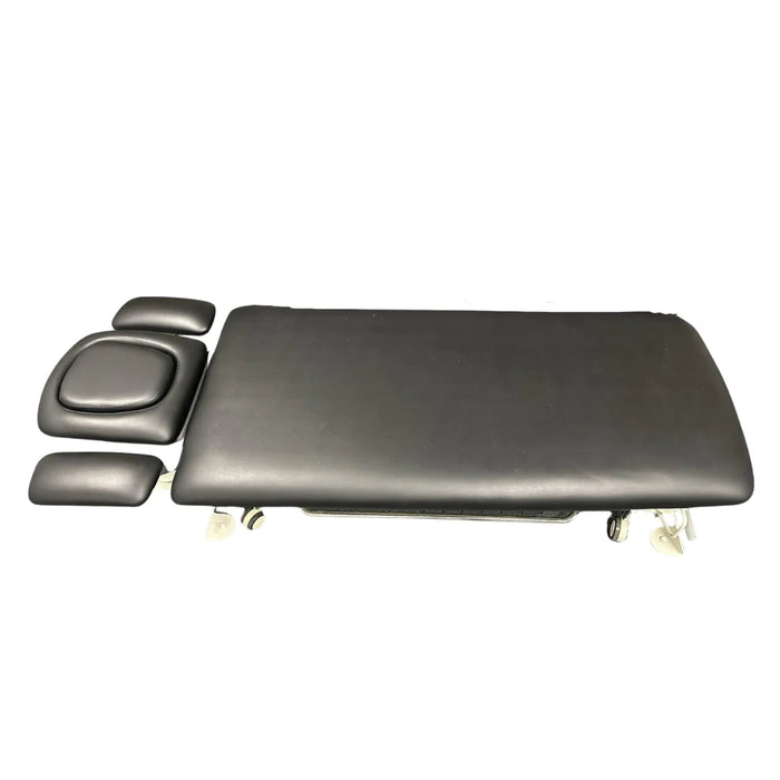 Portable massage and treatment table in black upholstery with detachable headrest, armrests, and wheels, side view from Therapy Supply