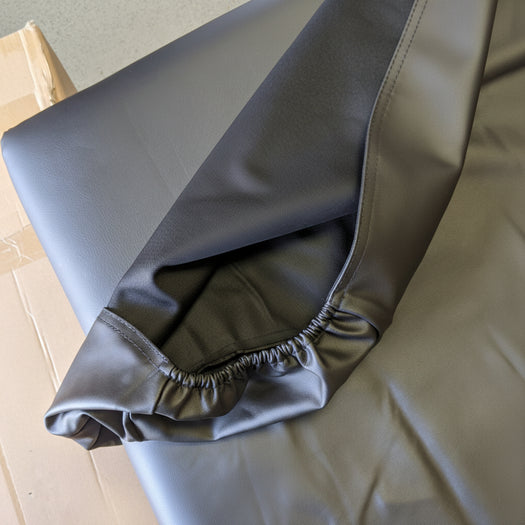 Detailed shot showing the durable black PU vinyl cover being fitted over the corner of a massage table, demonstrating the flexibility of the material.