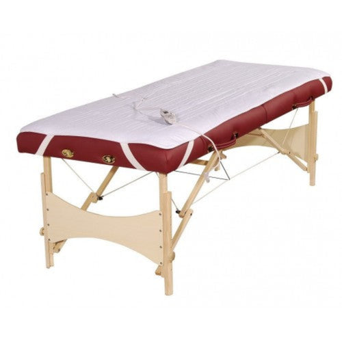Angled view of a portable wooden massage table smoothly fitted with the white fleece Deluxe Massage Table Warmer Pad, secured with elastic corner straps to eliminate cold surface shock for clients.