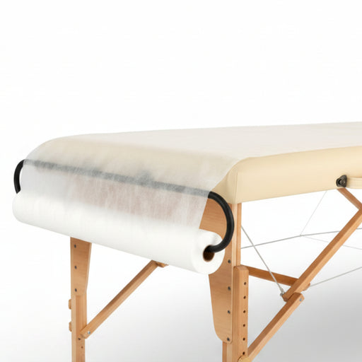 Angled view of a wooden massage table smoothly draped with the white Non-Woven Disposable Massage Table Sheets from a dispenser roll, providing a quiet, hygienic surface for clients.