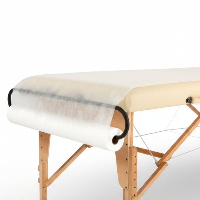 Angled view of a wooden massage table smoothly draped with the white Non-Woven Disposable Massage Table Sheets from a dispenser roll, providing a quiet, hygienic surface for clients.
